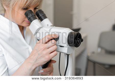 Young Female Professional Gynecologist In The Working Process, Looks Into The Colposcope.