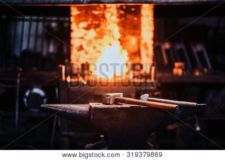Dark Stithy Workshop With Hammer On Anvil At Firs Plan And Fire In Stove At Background.