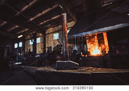 Dark Stithy Workshop With Hammer On Anvil At Firs Plan And Fire In Stove At Background.