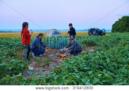 Family traveling and camping, twilight, cooking on the fire. Beautiful nature - field, forest and moon.