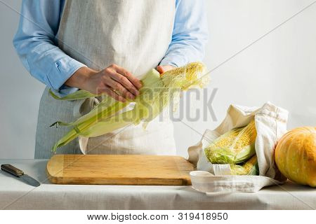 A Female Cook A Cotton Apron Cleans Ripe Corn On The Cob. Rustic Natural Style. The Concept Organic 