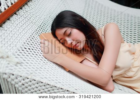 Young And Cute Asian Girl Lying In A Hammock With Book During Holiday