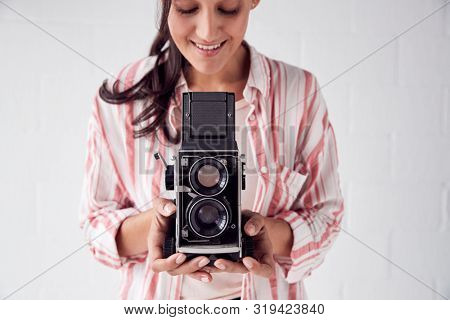 Female Photographer With Vintage Medium Format Camera On Photo Shoot Against White Studio Backdrop