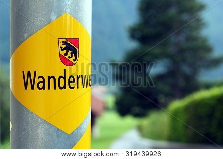 Aeschi, Switzerland - July 24, 2019: Yellow Hiking Path Signs In Bernese Oberland Show Hikers The Wa