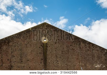 Wall Of An Old Abandoned House, Creating A Tringle With The Roof Line. Circular Hole In The Wall. Bl