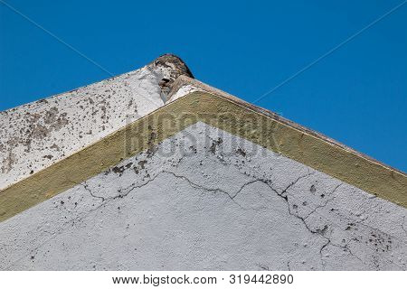 Wall Of An Old House, Creating A Tringle With The Roof Line. White Weathered Facade, Yellow Border. 