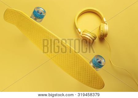 Yellow Headphones And Skateboard Or Pennyboard On Yellow Background. Music Concept.