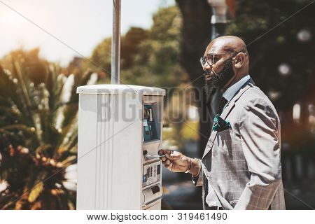 An Adult Confident Bald Black Man entrepreneur With A Beard And In Spectacles Is Using A Parking Pay