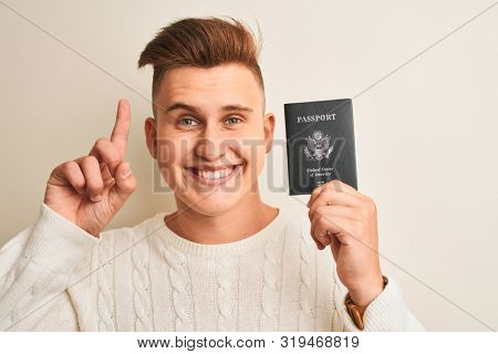 Young handsome man holding USA United States passport over isolated white background surprised with an idea or question pointing finger with happy face, number one