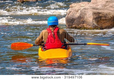 A Kayaker With Oars In Full Gear Is Sitting In A Kayak On White Water. Back View.