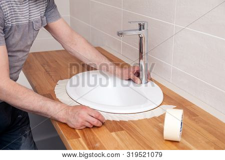 Closeup Hands Of A Professional Plumber Worker Installs A White Oval Ceramic Sink On A Wooden Tablet