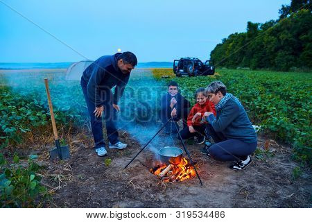 Family traveling and camping, twilight, cooking on the fire. Beautiful nature - field, forest and moon.