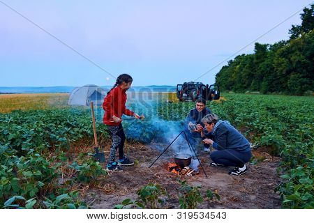 Family traveling and camping, twilight, cooking on the fire. Beautiful nature - field, forest and moon.