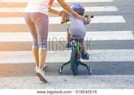 Mother Goes Pedestrian Crossing With Childr On Bicycle. A Woman With Son Crossing The Road In The Ci