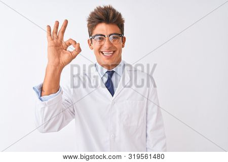 Young handsome sciencist man wearing glasses and coat over isolated white background smiling positive doing ok sign with hand and fingers. Successful expression.