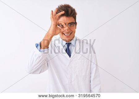 Young handsome sciencist man wearing glasses and coat over isolated white background doing ok gesture with hand smiling, eye looking through fingers with happy face.