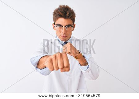 Young handsome sciencist man wearing glasses and coat over isolated white background Punching fist to fight, aggressive and angry attack, threat and violence