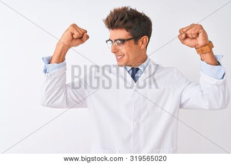 Young handsome sciencist man wearing glasses and coat over isolated white background showing arms muscles smiling proud. Fitness concept.