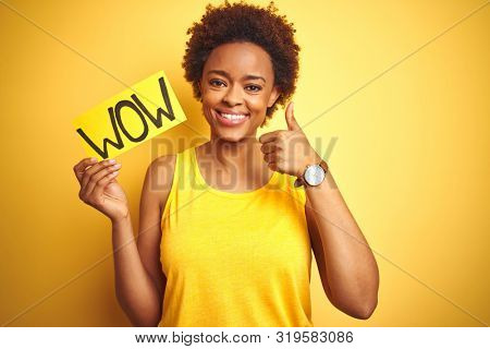 Young african american woman showing wow banner board over yellow isolated background happy with big smile doing ok sign, thumb up with fingers, excellent sign
