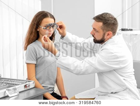 Doctor ophthalmologist holding special eye equipment examinating teenager girl's eyes in the clinic