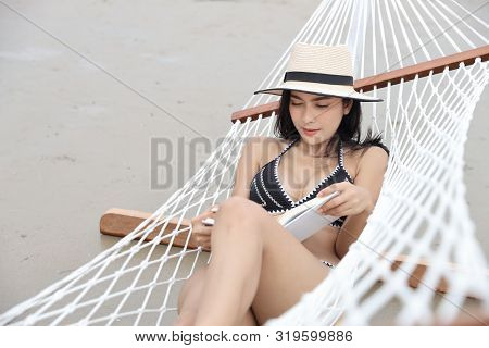 Sexy Asian Woman In Black And White Bikini Who Lying On Hammock And Reading Book On Sandy Beach With