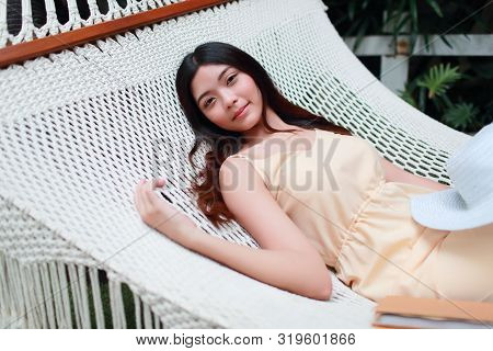 Young And Cute Asian Girl Lying In A Hammock With Book Beside During Holiday