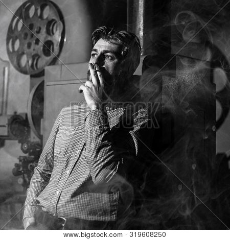 Black And White Photo Of A Tired Projectionist Smoking In A Movie Room. Everything Is In The Smoke. 
