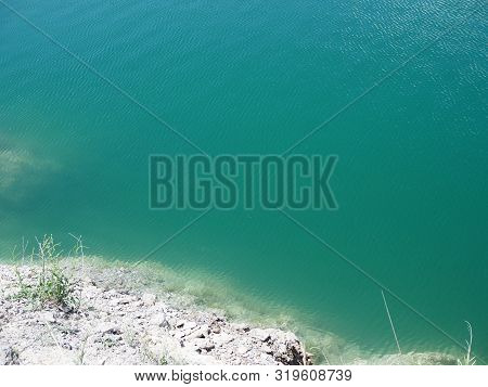 Top View Of The Clear Clear Water Of The Lake And The White Rocky Shore
