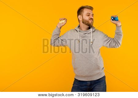 Attractive Man In A Gray Sweatshirt Joyfully Dances With A Credit Card In His Hand On A Yellow Backg