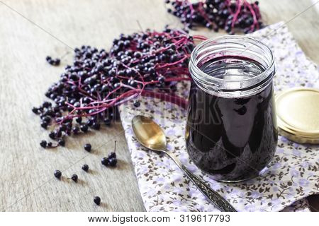Homemade Black Elderberry Syrup In Glass Jar And Bunches Of Black Elderberry In Background