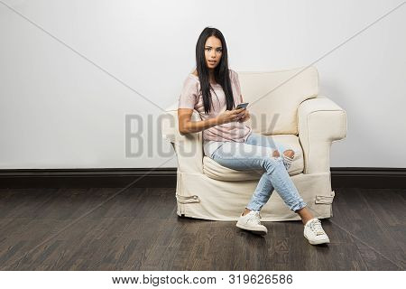 Twenty Something Brunette Woman, Sitting On A White Couch, Texting On Her Phone