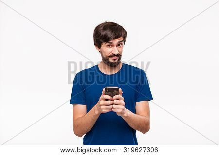 Good Looking Brunet Man In A Blue Shirt With Beard And Mostaches Shocked Holding Smartphone Looking 