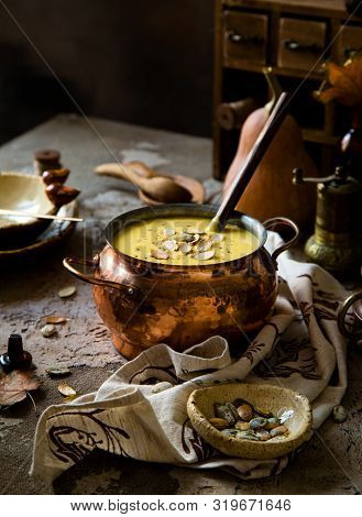 Pumpkin Yellow Soup Puree With Pumpkin Seeds On Top In Copper Pan On Rustic Concrete Table With Napk