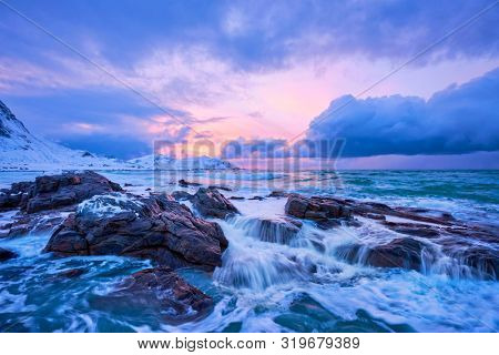 Waves of Norwegian sea on rocky coast in fjord on sunset. Skagsanden beach, Lofoten islands, Norway