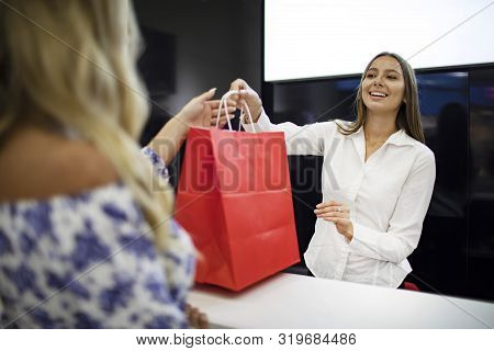 Blonde Customer Gets Her Trendy Purchases From Smiling Saleswoman Across A Counter