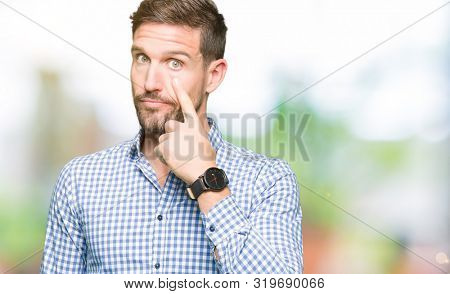 Handsome business man with blue eyes Pointing to the eye watching you gesture, suspicious expression
