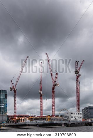 Amsterdam, The Netherlands - July 1, 2019: Construction Site With Four Tall Red Cranes Under Heavy R