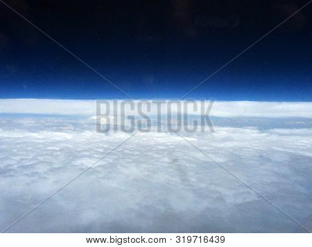 Aerial View Through Airplane Porthole Of A Deep Blue Sky Above A Sheet Of White Clouds