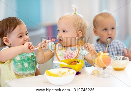 Babies Have Lunch In Creche. Kids Eating Healthy Food In Kindergarten. Funny Children Have A Dinner 