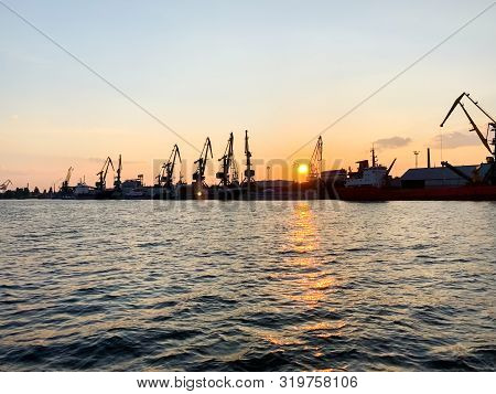 River Port With Ships At Sunset. Busy Traffic Artery. Logistics And Infrastructure. Loading And Unlo