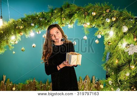 Girl With A Gift On The Background Of Christmas Decoration. Happy Woman With Gift Box In Christmas D