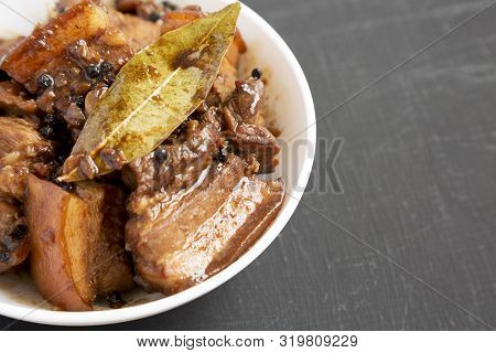 Homemade Filipino Adobo Pork In A White Bowl On A Black Surface, Side View. Space For Text.