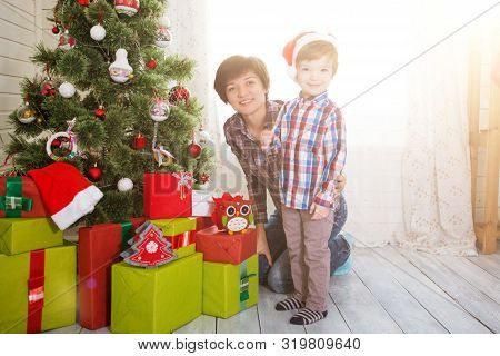 Smiling Mother With Her Beautiful Little Son Decroating Christmas Tree With Baubles At Home