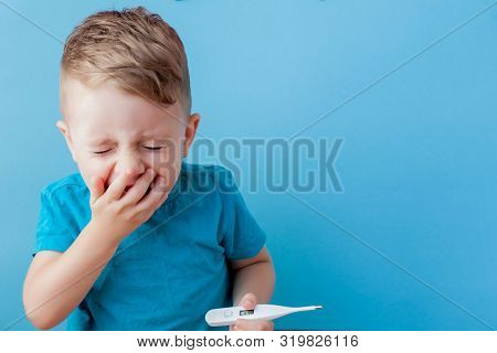 Ill Young Child With A Thermomether, Measuring The Height Of His Fever And Looking Into The Camera