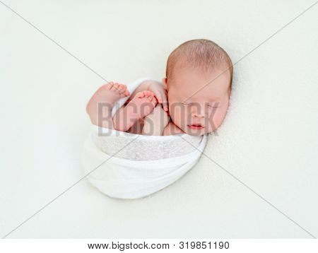 Newborn beatiful cute baby sleeping curled up in white blanket on white bed background
