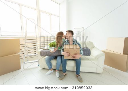 Moving And Real Estate Concept - Happy Couple Kissing On Sofa In Their New Flat