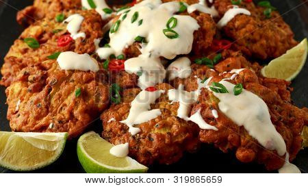 Indian Takeaway Food, Spicy Onion Bhajis Served With Chili Yoghurt Dip And Lime Wedges On Wooden Boa