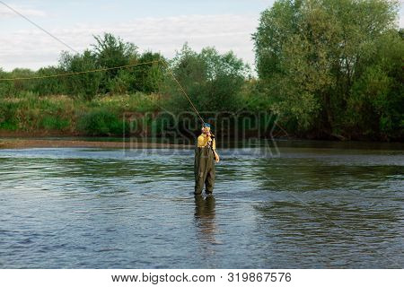 Fishermen Are Standing In The River, Wearing Rubber Boots. Men Throw Fishing Rods. Fishing Adventure