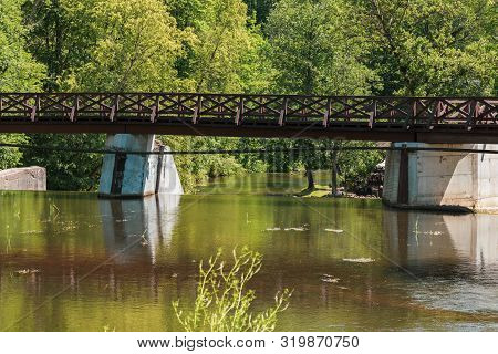 Wooden Bridge Over The River Vilia In Vilnius With A Waterfall In The Park Belmonto.