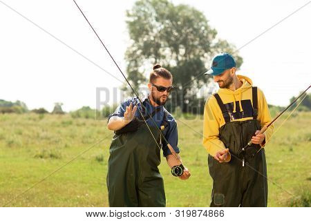 Two Fishermen Preparing For Fishing. They Hold The Fishing Rods And Talk To Each Other. Sport Fishin